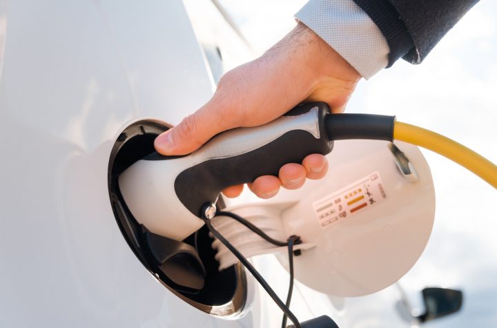 Close up man in the suit plugging a power supply into an electric car at charging station in the