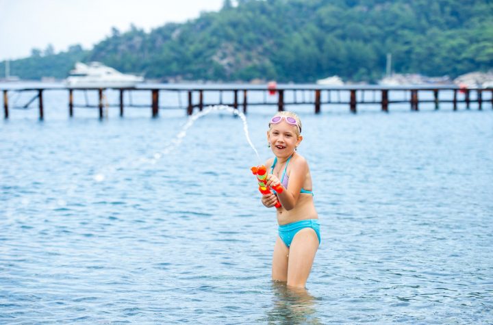 Adorable little girl is swimming in the sea and playing with a water gun. Turkey