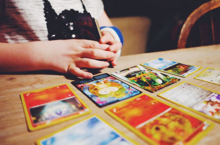 Child sitting by a table top playing with Pokémon cards without her face is shown