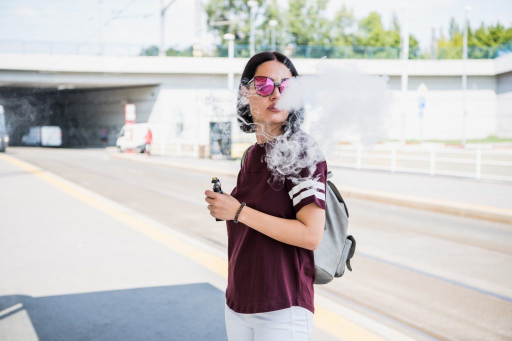 Stylish girl smoking an e-cigarette as she is walking through the city.