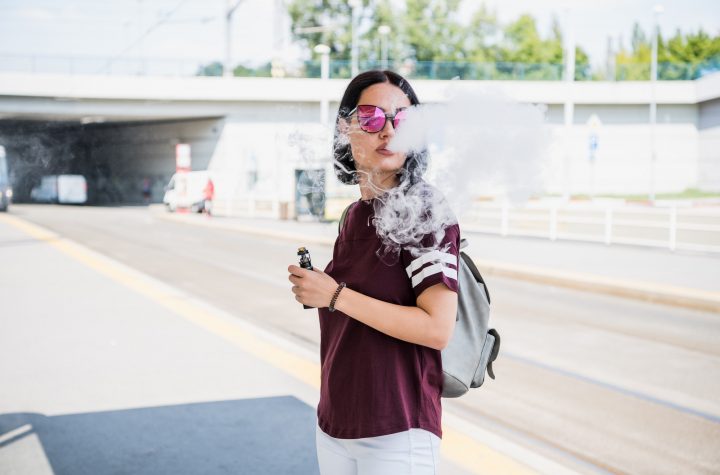Stylish girl smoking an e-cigarette as she is walking through the city.