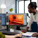 Multiethnic women designer looking at computer with dual displays