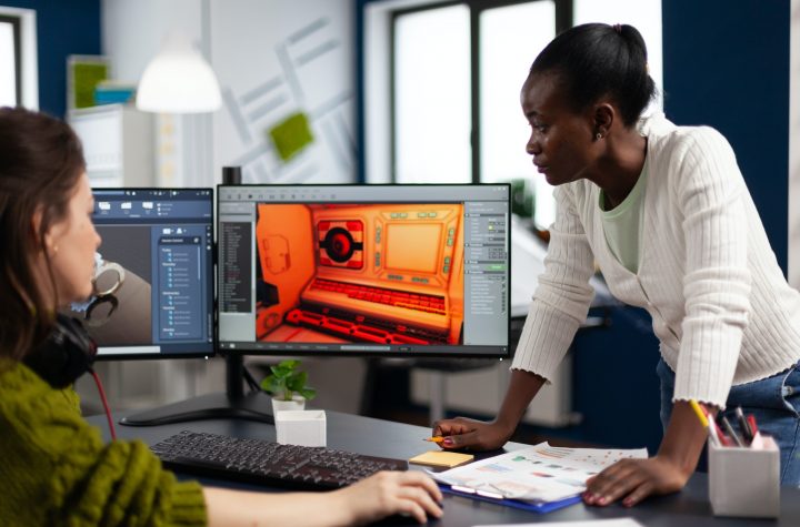 Multiethnic women designer looking at computer with dual displays