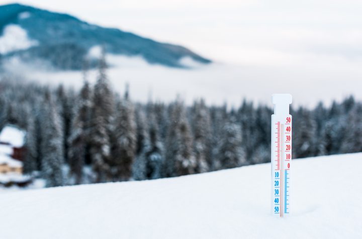 thermometer in snowy mountains with pine trees and white fluffy clouds