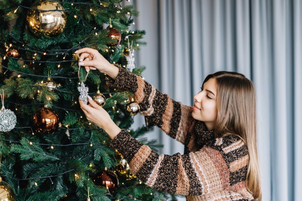 Young woman decorates the Christmas tree with toys. Preparing for the holidays