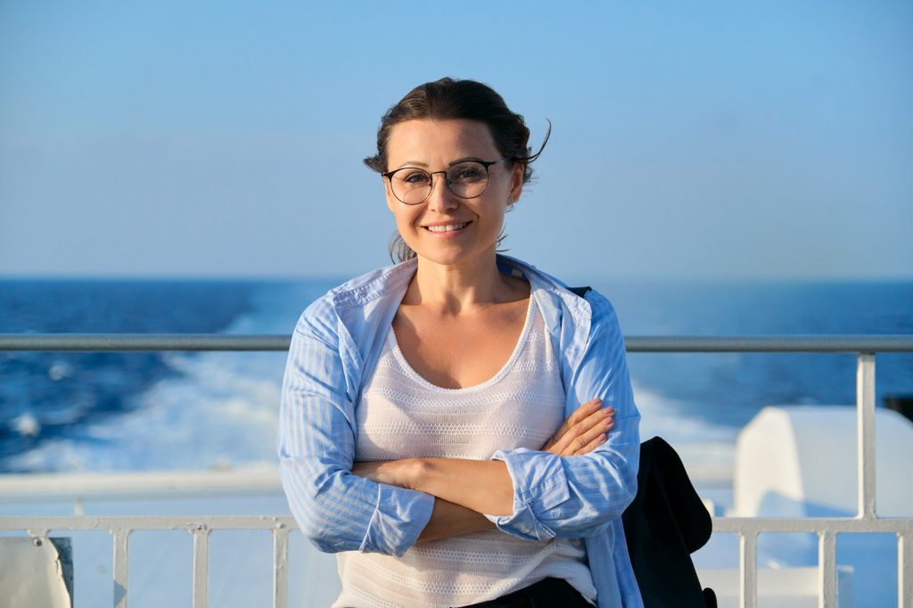 Female in blue shirt on the deck of ship looking at camera, sky sea sunset background