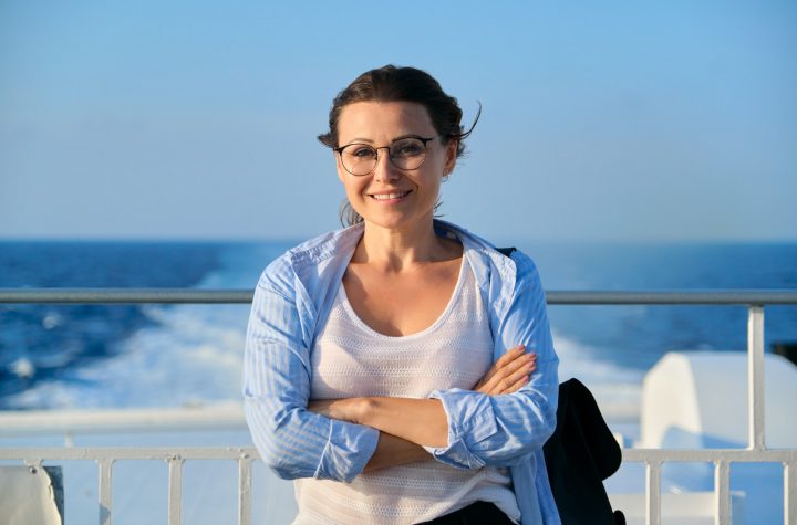 Female in blue shirt on the deck of ship looking at camera, sky sea sunset background