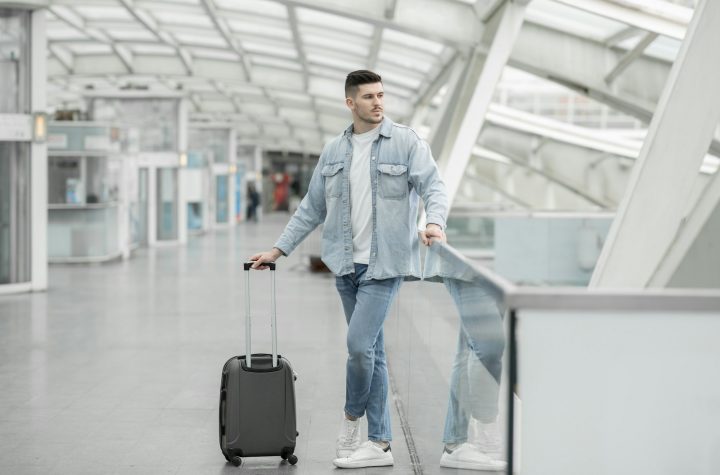 Male Passenger With Travel Suitcase Waiting For Flight In Airport