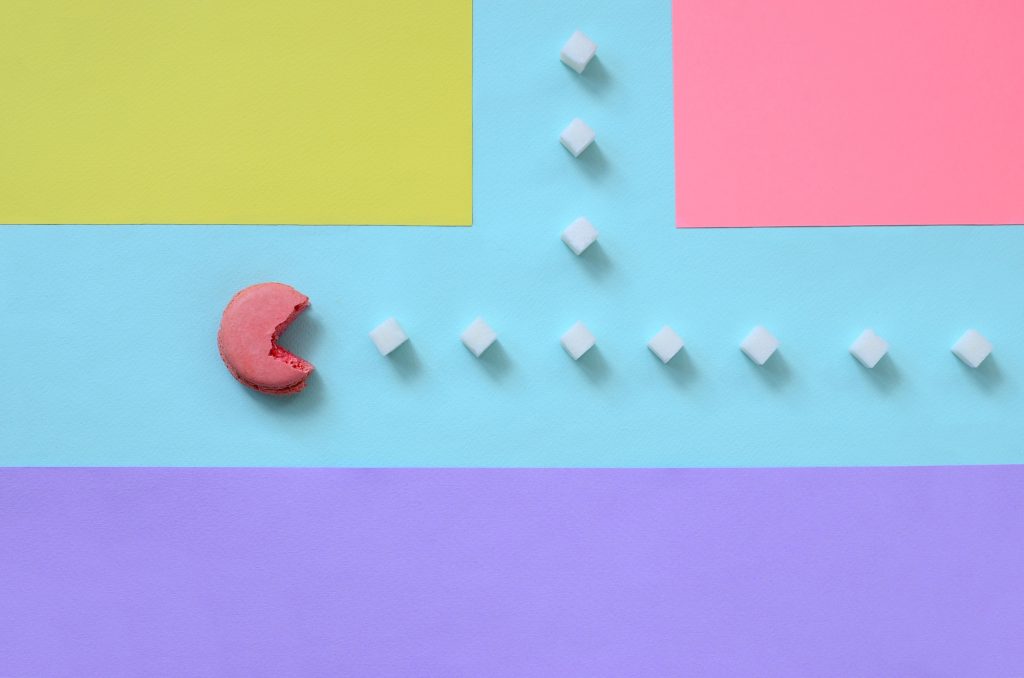 Macaroon Pac Man eats sugar cubes on pastel colored paper