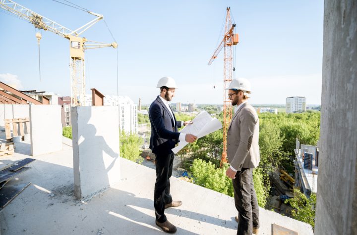 Two engineers or architects supervising the process of residential building construction standing on the structure outdoors
