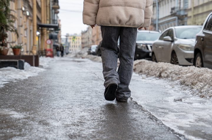 Pedestrian walking on slippery sidewalk rear view. Pavement covered with slippery ice. Frozen rain. Winter time.