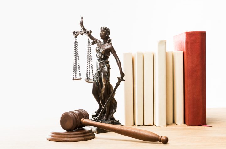 figurine with scales of justice, brown gavel and books on wooden table isolated on white