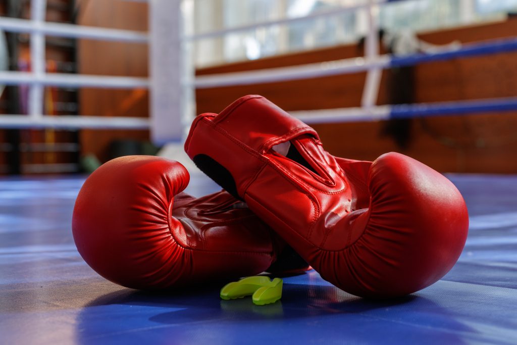 Closeup of red boxing gloves with mouthguard on a blue ring canvas in gym light, ideal for training fight sport gear themes.
