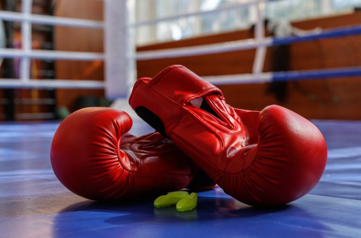 Closeup of red boxing gloves with mouthguard on a blue ring canvas in gym light, ideal for training fight sport gear themes.