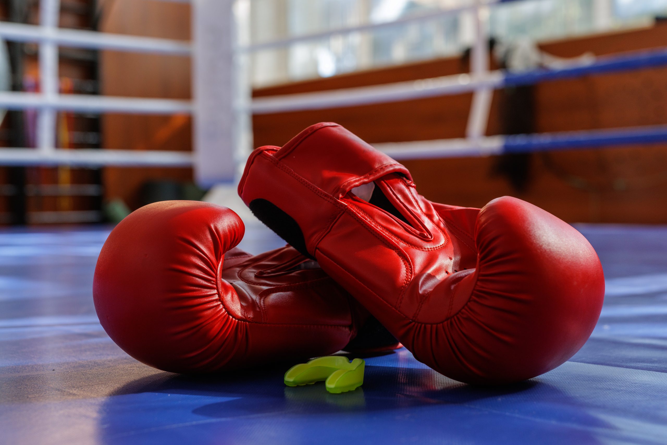 Closeup of red boxing gloves with mouthguard on a blue ring canvas in gym light, ideal for training fight sport gear themes.
