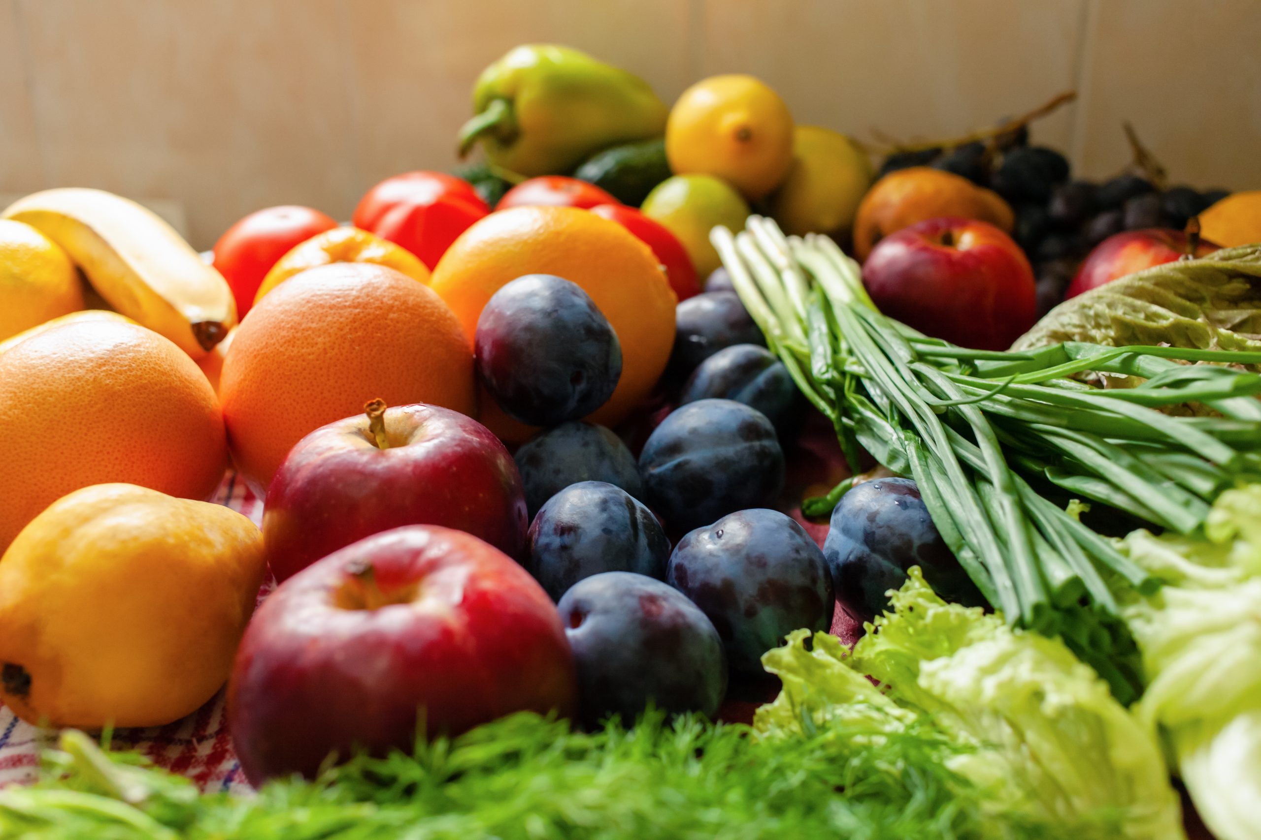 Fruits, vegetables and greens lie on the table, natural light from the window.