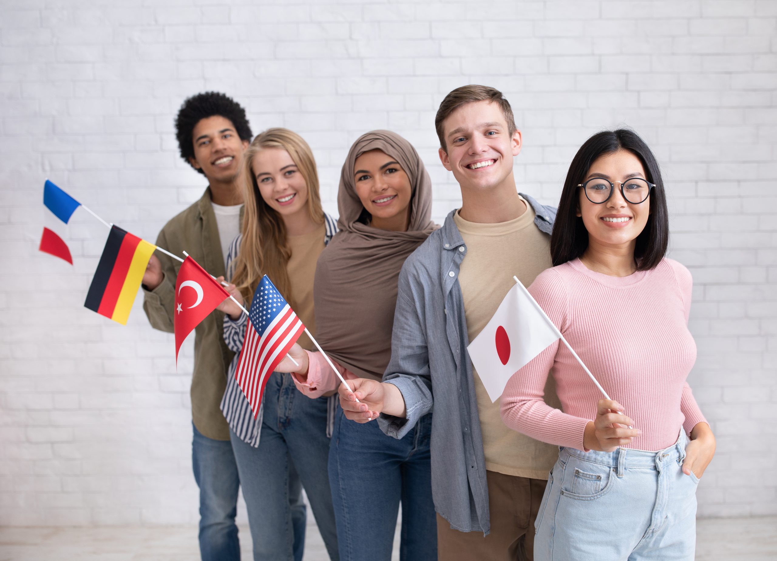 Exchange students and language school for different people. Funny digital young international pupils holding flags of USA, Japan, Turkey, Germany and France in classroom, studio shot, empty space, Menschen mit verschiedenen Fahnen, Ausländer